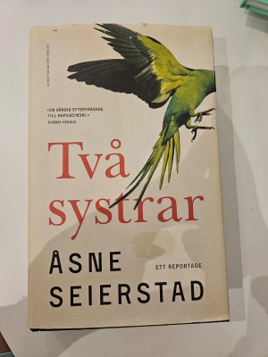 Två systrar  - Två systrar av Åsne Seierstad är en reportagebok med beige omslag och en grön papegoja på framsidan. Boken utforskar två norska tonåringars radikalisering och resa till Syrien. Perfekt för dig som gillar samhällsfrågor och verklighetsbaserade berättelser.