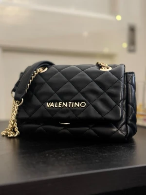 Valentino väska  - Svart quiltad handväska från Valentino med guldfärgade kedjedetaljer och logotyp framtill. Säljer för att den inte kommer till användning. Sparsamt använd och är i princip i nyskick. Fick den i present därav inget kvitto. För frågor eller fler bilder får ni gärna höra av er 💕