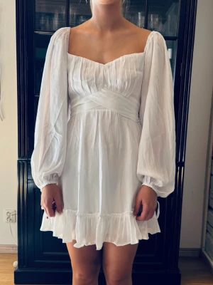 Ny vit studentklänning. S. Hello Molly. NWT. Klänning.  - Ny superfin vit klänning med långa puffärmar, markerad midja och volangkant nertill. Perfekt till studenten. Storlek S. Från Hello Molly. Jättefin kvalitet på tyget, med snyggt fall. Fodrad förutom i ärmarna. Dragkedja bak. Många fina detaljer. Dyr i inköp o vi bestämde för sent att den inte skulle användas. Oanvänd. Lappen kvar. Finns inget att anmärka på. NWT.