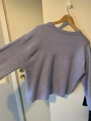 Ljuslila stickad tröja från 157 - Mysig ljuslila stickad tröja från 157 med rund halsringning och avslappnad passform. Tröjan har ribbstickade muddar vid halsen och är perfekt för lager-på-lager-stil. Enkel och stilren design som passar till många outfits. Passar som Xs S M