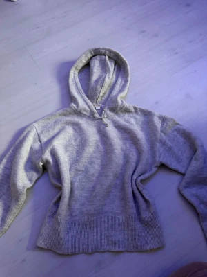 Grå stickad hoodie med huva - Mysig grå stickad hoodie med bred ribbad mudd nertill och vid ärmslut. Hoodien har en klassisk huva och avslappnad passform, perfekt för en chill och avslappnad stil. Materialet känns mjukt och skönt mot huden. Stolek 170 men passar S/M