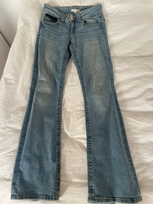 Blå bootcut jeans  - Snygga ljusblå bootcut jeans från Gina Tricot Young med dubbla knappar i midjan och klassiska fickor fram och bak. Jeansen har en lätt utsvängd passform och är gjorda i denim med synliga sömmar. 