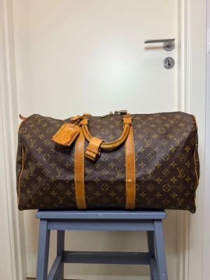 Louis Vuitton Keepall - Louis Vuitton Keepall 50  SKICK • Generellt: Fint vintage skick • Canvas: Fint vintage skick • Vachetta: Fint skick • Metaldetaljer: Patina • Zipper: Fungerande • Handtag: Fint skick • Hörn: Fint skick • Insida: Fint skick. • Date code: 874 • Övrigt: En popnit saknas vid ena handtaget. Se bild. Nyckel saknas. • Mått: H28 B50 D21