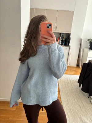 Ljusblå stickad tröja med rund hals - Mysig ljusblå stickad tröja med rund hals och långa ärmar. Tröjan har ribbstickade muddar vid ärmslut och nederkant, vilket ger en avslappnad och trendig look. Perfekt för att hålla sig varm under kyliga dagar.