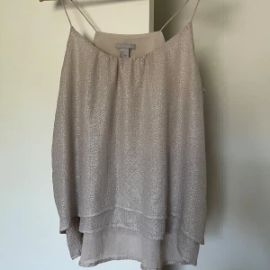 Glittrig champagnefärgad linnetopp - Säljer en glittrig champagnefärgad linnetopp. Toppen har tunna axelband, dubbla lager tyg och ett luftigt fall. Perfekt för dig som vill ha en stilren men ändå festlig look.