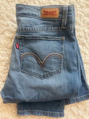 Levi's ljusblå slitna jeans - Säljer ett par ljusblå jeans från Levi's med klassisk femficksdesign och slitningar på båda knäna.  Perfekta för en avslappnad och trendig look.