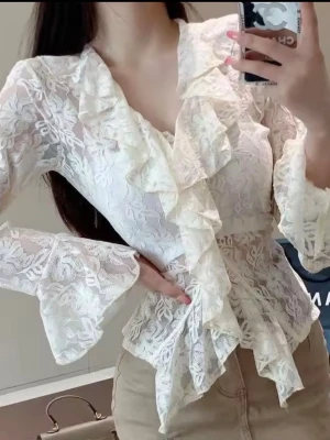 Creamfärg  spetsblus med volanger - Superfin spetsblus med långa ärmar och volangdetaljer längs framstycket och ärmsluten. Blusen har en feminin v-ringning och är tillverkad i transparent spetsmaterial med blommigt mönster. Perfekt för en trendig och romantisk look.