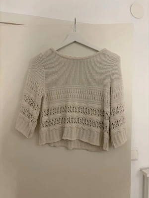 Beige stickad topp med spetsdetaljer - Säljer en beige stickad topp med trekvartsärm och vackra spetsdetaljer i mönstret. Tröjan har en lös passform och är tillverkad i ett mjukt, tunt material som känns luftigt. Perfekt för lager på lager och ger en romantisk touch till din outfit.