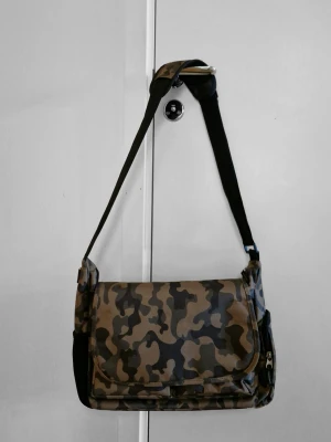 Axelremsväska/datorväska med camoflagemönster - Väldigt många år gammal men fortfarande i bra skick. Allt fungerar. Har flera fickor lite överallt och justerbar axelrem. 