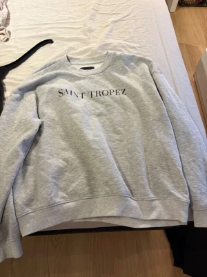 Grå sweatshirt Saint Tropez - Sweatshirt med ett tryck (saint tropez). Den är använd ganska mycket så det finns några knottror på den.