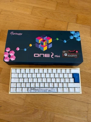 Ducky One 2 Mini mekaniskt tangentbord - Säljer ett Ducky One 2 Mini mekaniskt tangentbord i vitt med blåa detaljer. Kompakt 60%-layout, USB-anslutning och extra keycaps samt verktyg medföljer. Tangentbordet har unika tryck på mellanslagstangenten och är perfekt för gaming eller skrivande.