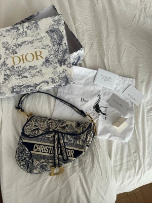 Dior Saddle Bag - Säljer en ikonisk Dior Saddle Bag i blått och vitt med detaljerat mönster och guldiga metalldetaljer. Bara att skicka om det skulle vara några funderingar🤍