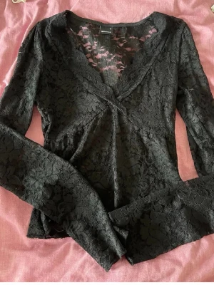 Svart spetströja från Gina Tricot - Säljer en svart långärmad spetsblus från Gina Tricot. Blusen har v-ringning, omlottdesign och är helt täckt av blommig spets. 