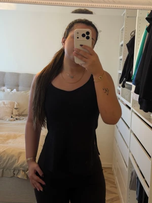 Svart linnetopp med smala axelband - Säljer en svart linnetopp med smala axelband och enkel, stilren design. Toppen har en något lös passform och är perfekt för varma dagar eller som lager under en skjorta. Passar dig som gillar minimalistisk stil.