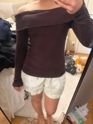 Mörkbrun offshoulder ribbad topp - Säljer en mörkbrun, ribbad offshoulder topp med lång ärm. Toppen har en bred kant över axlarna och sitter tight mot kroppen för en snygg siluett. Perfekt för dig som gillar stilrena och trendiga plagg.