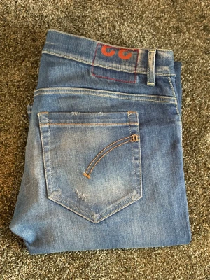 Dondup George jeans - Ett par blå skinny jeans med slitna detaljer och hål på benen. Jeansen har klassisk femficksdesign, kontrastsömmar och en liten broderad detalj på bakfickan. Tillverkade i denim med stretch för skön passform.