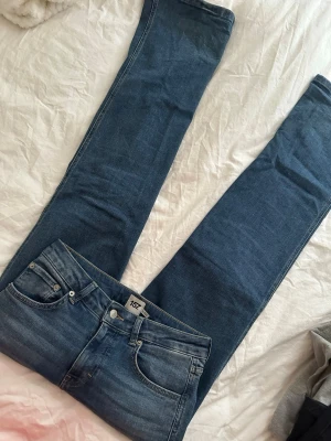 Blå utsvängda low waist  jeans från 157 - Säljer ett par klassiska blå jeans från 157 med utsvängd  passform och fem fickor. Jeansen har normal midja, silverfärgade knappar och nitar samt subtila slitningar för en avslappnad look. Perfekta till vardags och lätta att matcha med olika stilar.