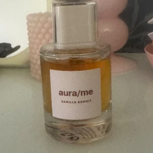 aura/me Vanilla Addict parfym - Upptäck aura/me Vanilla Addict, en parfym i en rund glasflaska med silverfärgat lock. Doften har en tydlig vaniljkaraktär och flaskan har en stilren vit etikett med vinröd text. Perfekt för dig som älskar söta och varma dofter.