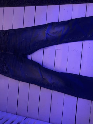 Replay anbass - Säljer ett par mörkblå slim fit jeans från Replay med slitningar och lätt tvättade detaljer. Klassisk femficksmodell med knappgylf och raka ben. Perfekta för en avslappnad och trendig stil. Materialet är bomull med lite stretch för extra komfort.