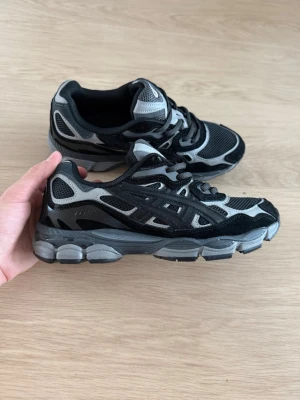 Svarta och grå Asics sneakers - Säljer ett par snygga Asics sneakers i svart och grått med mesh- och syntetpaneler. Skorna har en chunky sula och klassisk snörning. Perfekta för dig som gillar sportig och trendig stil. Asics-logga på sidan och bak.