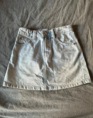 Ljusblå jeanskjol med fickor - Säljer en ljusblå jeanskjol i kort modell med klassiska fem fickor, bälteshällor och knappstängning fram. Kjolen har en rak passform och är perfekt för en avslappnad stil. Märket syns på bakre etiketten. Superfin till sommaren🌸🌸🌸