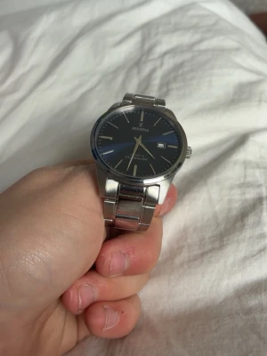 Festina klocka med blå urtavla - Stilren klocka från Festina med mörkblå urtavla och datumvisning. Armbandet är i silverfärgad metall och har en klassisk länkdesign. Perfekt accessoar för dig som gillar en tidlös look.