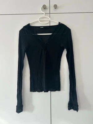 Svart långärmad topp från Bik Bok - Säljer en svart långärmad topp från Bik Bok med v-ringning och spetsdetaljer vid halsringningen och ärmsluten. Toppen har en slim passform och är tillverkad i ett mjukt, stretchigt material som sitter snyggt på kroppen. Ordinarie 299kr pris 150kr