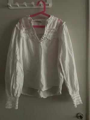Vit blus med smock från Holly & Whyte - Vit blus från Holly & Whyte by Lindex med långärmad design, smockdetaljer vid ärmslut och axlar samt v-ringad hals. Blusen har ett luftigt tyg och dekorativa broderier upptill. Perfekt för en trendig och avslappnad look. Tröjan är använd endast ett fåtal gånger eftersom den är för liten. Storlek S men passar till M med. Pris går att diskutera! ❤️