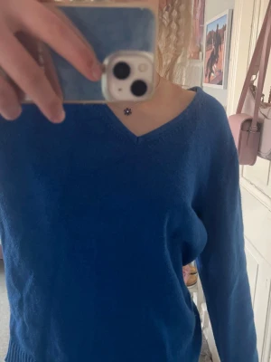 Blå stickad tröja med V-ringning - En enkel och snygg blå stickad tröja med V-ringad hals och långa ärmar. Tröjan har ribbstickade muddar vid ärmslut och nederkant. Perfekt att slänga på sig när det är lite kyligare ute.