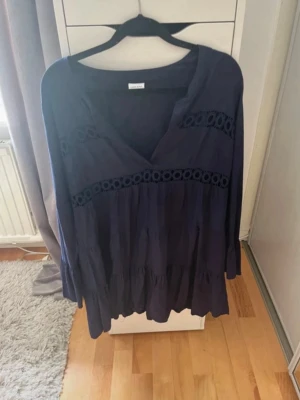 Marinblå långärmad klänning med spets - Säljer en marinblå klänning med v-ringning och långa ärmar. Klänningen har fina spetsdetaljer över bröstet och midjan samt volang nedtill. Perfekt för dig som gillar en avslappnad men ändå stilren look. Kan skicka bild med klänningen på vid förfrågan.