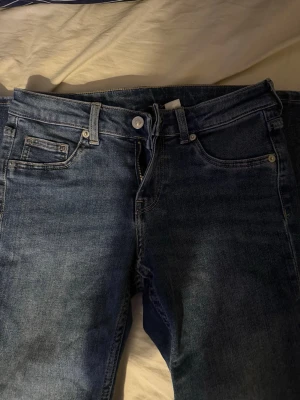 Lowaist jeans  - Säljer ett par klassiska mörkblå jeans med utsvöbgd passform och fem fickor. Jeansen har låg midja, bälteshällor och stängs med knapp och dragkedja. Materialet är denim i bomull och de har en snygg tvättad look.