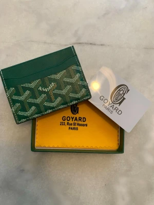 Grön kortfodral från Goy4ard - Snyggt grönt kortfodral från Goy4ard med det klassiska mönstret i vitt och beige. Tillverkad i canvas och läder, perfekt för kort och ID. Kommer med original ask och tygduk. Stilren och exklusiv accessoar från Paris.