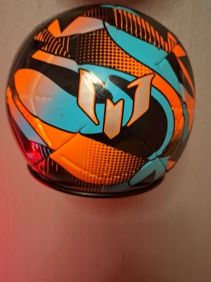 Adidas Messi fotboll storlek 3 - Snygg Adidas Messi fotboll i storlek 3 med färgstarkt mönster i svart, orange och turkos. Bollen har Messi-loggan tryckt på ena sidan och är perfekt för träning eller spontanspel. Tillverkad i slitstarkt syntetmaterial.