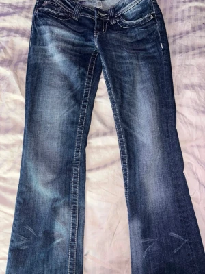 Blå bootcut miss me jeans - Säljer ett par blå bootcut miss me jeans med snygga slitningar och broderade detaljer på bakfickorna. Jeansen har vita kontrastsömmar. Säljer pga att dem är för stora för mig. Använd typ 3 gånger. Klassisk femficksmodell i mjuk denim.