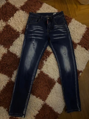 Dsquared2 jeans  - Snygga mörkblå dsquared2 slim fit jeans med coola slitningar och blekta detaljer på både fram- och baksidan. Klassisk femficksdesign och knappstängning. Perfekta för dig som gillar snygga slim fit jeans. Bara att skriva om du har frågor.
