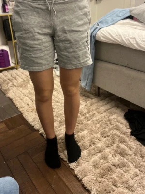 Grå sweatshorts från Sail Racing - Grå sweatshorts från Sail Racing med snörning i midjan och logga på sidan. Mjukt och bekvämt material i bomull, perfekt för chill dagar. Klassisk passform och midwaist. Snygga att matcha med en hoodie eller t-shirt.