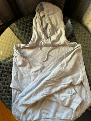 Ljusblå hoodie med huva - En enkel och stilren ljusblå hoodie med huva och dragsnören. Hoodien har en klassisk känguruficka framtill och ribbade muddar vid ärmslut och nederkant. Perfekt för en avslappnad och casual look.