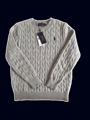 Polo Ralph Lauren Cable Knit Sweater - Snygg grå kabelstickad tröja från Polo Ralph Lauren med rund halsringning och klassisk broderad logga på bröstet. Tröjan är i storlek S