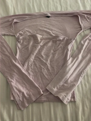 Ljusrosa offshoulder topp - Trendig ljuslila offshoulder topp med långa ärmar och figurnära passform. Tillverkad i mjukt material som känns skönt mot huden. Perfekt för dig som vill ha en stilren och modern look.