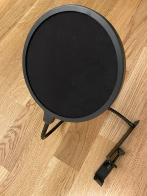 Svart popfilter till mikrofon - Säljer ett runt svart popfilter med metallram och flexibel arm. Fästet är i metall och har en skruv för enkel montering på mikrofonstativ. Perfekt till streaming, podd eller inspelning.