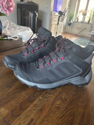 Gore tex vandrings känga  - Snygga svarta kängor med robust sula och röda detaljer på snörningen. Tillverkade i slitstarkt syntetmaterial och mesh för bra andningsförmåga. Vattentäta. Perfekta för utomhusaktiviteter och har en sportig look med hög komfort, ger bra stöd för ankeln. Endast använda 2 ggr. Nypris 1000;- 