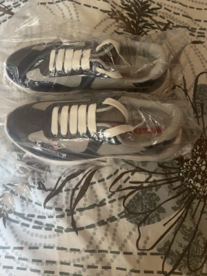 Blå och vita sneakers med Prada design - Snygga sneakers i blått och vitt med vita skosnören och meshpaneler för extra andningsförmåga. Skorna har en sportig look med blanka blå partier och en tjock vit sula. Perfekta för dig som gillar en fräsch och modern stil.