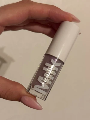 Lila glittrigt läppglans från Milk - Säljer ett läppglans från Milk Makeup i en snygg lila nyans med skimrande glittereffekt. Kommer i en genomskinlig tub med vit kork och tydlig logga. Perfekt för dig som vill ha glansiga och glittriga läppar. Ny och oanvänd.
