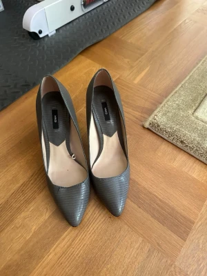 Grå pumps med ormmönster från Mango - Snygga grå pumps från Mango med spetsig tå och hög klack. Skorna har ett diskret ormmönster i materialet. Använda 2 gånger super bekväma och fina. Nypris är 600kr