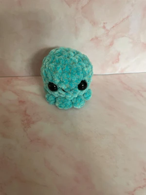 Blå spräcklig virkad bläckfisk plushie - Supersöt liten bläckfisk i blått, virkad med mjukt garn och stora svarta ögon. Perfekt som dekoration eller gosedjur. Den har en rund form och små ben som sticker ut runt om kroppen. 6,5cm hög