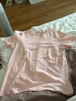 Ljusrosa basic t-shirt - En enkel och stilren ljusrosa t-shirt i mjuk bomull. T-shirten har rund halsringning och korta ärmar, perfekt för en avslappnad look. Passformen är normal och tyget känns skönt mot huden. Original priset är 300kr