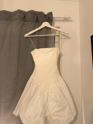 Vit kort klänning från Gina Tricot - Supersöt vit klänning från Gina Tricot med tunna axelband och puffig kjol. Klänningen har en enkel, stilren överdel och ballongformad nederdel!