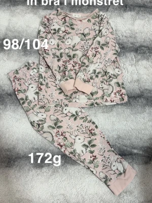 Rosa pyjamas med djurmotiv - Supersöt rosa pyjamas med långärmad tröja och byxor, täckt av ett gulligt mönster med vita kaniner, ekorrar och blommor. Mjuka muddar vid ärmar och benslut. Perfekt för mysiga kvällar hemma.🌸 En fläck som smälter in bra i mönstret. Storlek 98/104