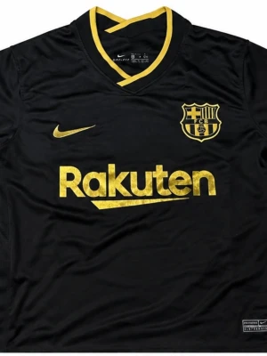Svart FC Barcelona matchtröja Nike - Snygg svart FC Barcelona matchtröja från Nike med guldiga detaljer och loggor. Tröjan har V-ringning med gul kant, tryckt Rakuten-logo på bröstet och klubbmärke i guld. Tillverkad i lätt och ventilerande material, perfekt för fotboll eller träning.
