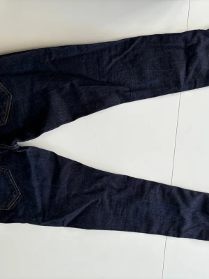 Mörkblå smala jeans med kontrastsömmar - Säljer ett par mörkblå jeans med smal passform och snygga kontrastsömmar. Jeansen har klassiska bakfickor och bälteshällor. Materialet är denim och de har en enkel, stilren look som passar till det mesta.